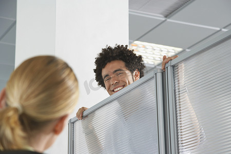 微笑的男性上班族凝视着隔间的墙壁，迎接办公室里的金发同事