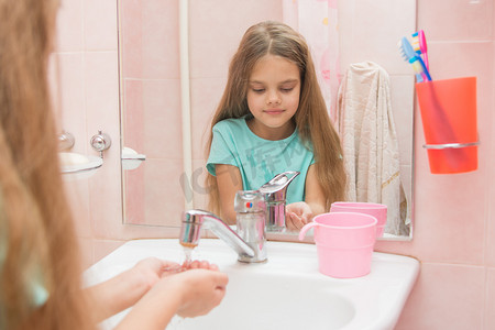 洗眼睛摄影照片_女孩在浴室里倒她的手自来水