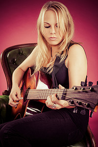 坐弹吉他摄影照片_金发女人坐着弹吉他