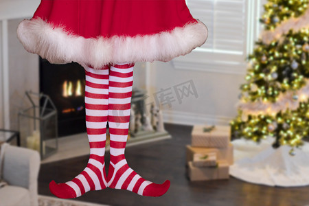 穿着条纹长袜的可爱圣诞精灵小女孩站在装饰精美的圣诞客厅里，背景是礼物和圣诞树