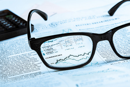 金融理财app个人中心摄影照片_金融图表和图表货币透过金融报纸上的眼镜镜片
