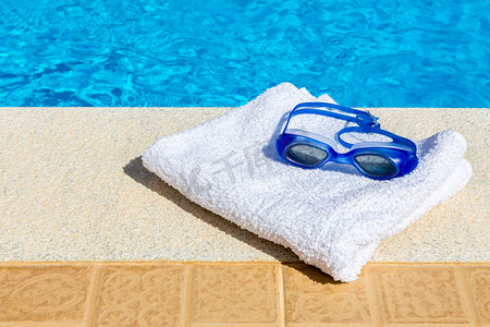 热毛巾摄影照片_游泳池附近的游泳镜和毛巾