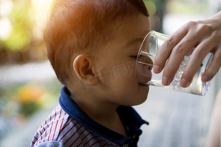 进入水里摄影照片_亚洲男孩正在从他进入的透明玻璃杯里喝水