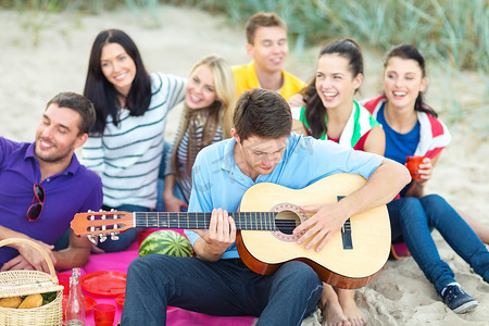 沙滩聚会摄影照片_一群快乐的朋友在沙滩上弹吉他