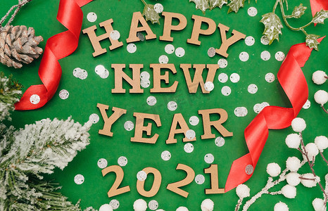 2021年新年快乐。绿色背景中新年帽上的木字，上面有红丝带、银色纸屑和云杉枝。节日装饰或明信片概念。顶视图和平铺 复制空间
