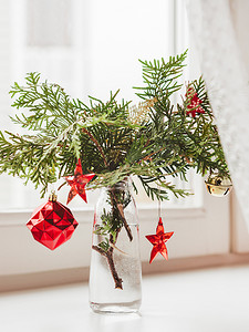圣诞节花瓶摄影照片_窗台上放着装饰着崖柏枝条的花瓶。