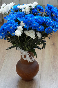 花瓶蓝色摄影照片_地板上的粘土花瓶里放着一束蓝色和白色的菊花