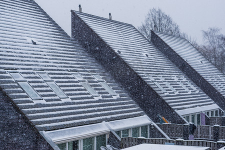 冬季雪、雪和寒冷天气覆盖的现代尖顶屋顶，新的荷兰房屋建筑