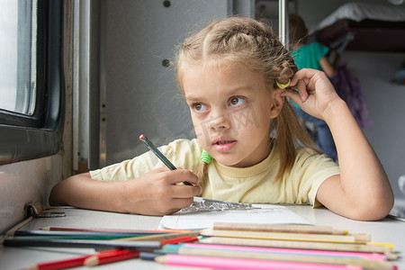 六岁女孩陷入沉思，看着窗外在二等火车车厢里画铅笔