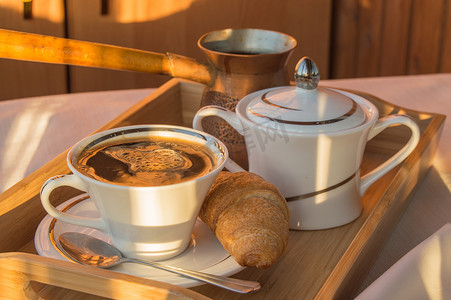 木盘上的美味经典早餐 — 复古铜 cezve、一杯咖啡和羊角面包，黎明背景