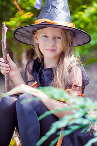 万圣室外摄影照片_可爱的小女孩在秋天的万圣节穿着女巫服装。