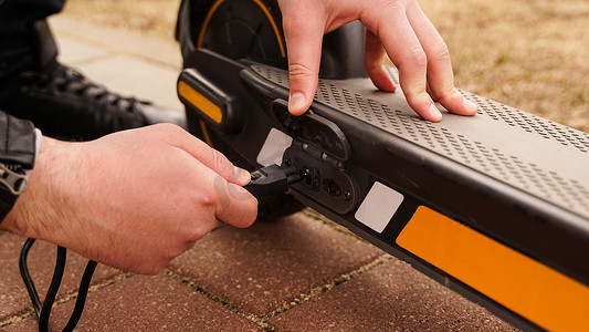 男子在特殊停车场用充电器为他的电动滑板车充电。
