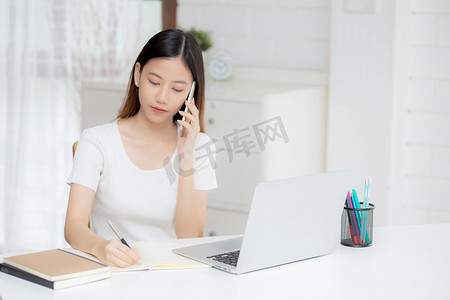 年轻的亚洲女性通过笔记本电脑在家打电话和工作，自由职业者在笔记本上写作并在智能手机上讲话，待在家里，家庭生活，商业和沟通理念。
