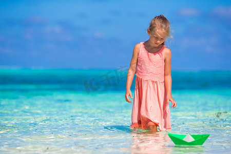 在绿松石海中玩纸船的可爱小女孩