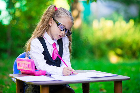书桌前可爱的小女生，有户外的笔记和铅笔。