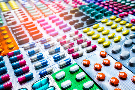 禁忌症摄影照片_五颜六色的片剂和胶囊药丸在泡罩包装中排列着美丽的图案和耀斑光。