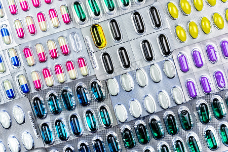 五颜六色的片剂和胶囊药丸在泡罩包装中排列着美丽的图案和耀斑光。