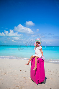 戴手套冬天摄影照片_戴着暖冬帽和手套的可爱女孩带着行李在海滩上散步