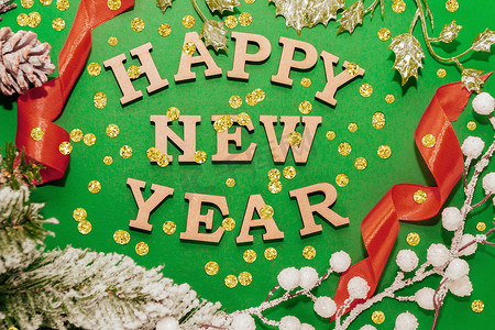 新年快乐。绿色背景中新年帽中的木字，带红丝带、金纸屑和云杉枝。节日装饰或明信片概念。顶视图和平铺 复制空间