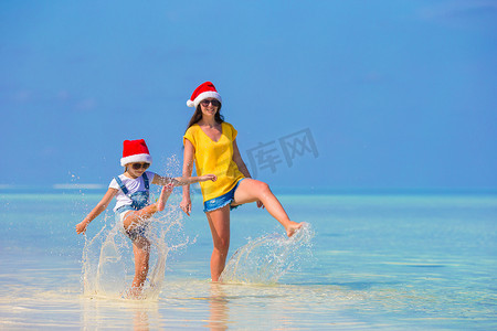 海滩度假期间戴着圣诞帽的小女孩和年轻母亲