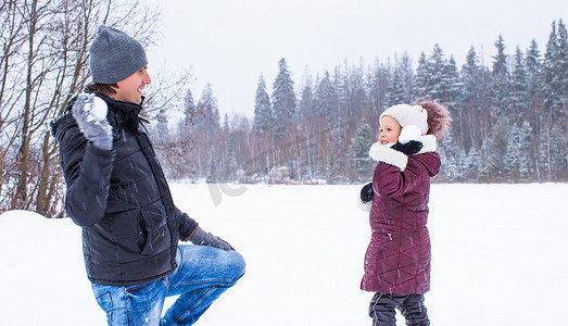 快乐的父亲和小女孩在冬天的雪天玩雪球