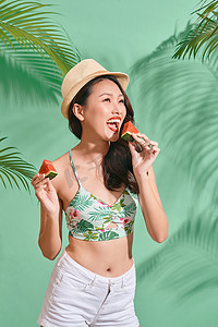蓝色背景中时尚漂亮的亚洲女人正在吃一片西瓜