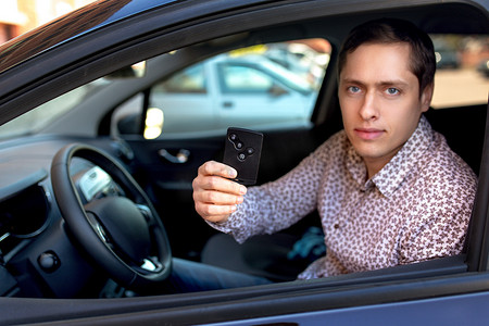防盗摄影照片_男人从车窗往外看，拿着汽车防盗钥匙