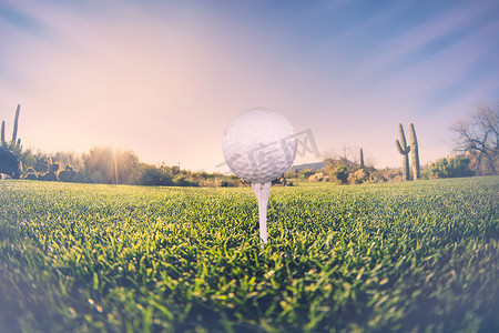 广角推理摄影照片_高尔夫球在发球台上的超广角视图，沙漠球道和背景中令人惊叹的亚利桑那日落