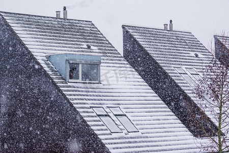 雪屋顶摄影照片_冬季被雪覆盖的尖尖屋顶，下雪的天气，现代荷兰建筑