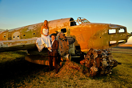 年轻的新婚夫妇站在坠毁的达科他州旧战机旁