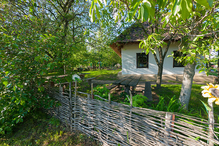 绿色栅栏摄影照片_一栋白墙、白墙、茅草屋顶和整洁窗户的房子矗立在用木栅栏围起来的绿草地上的院子里。