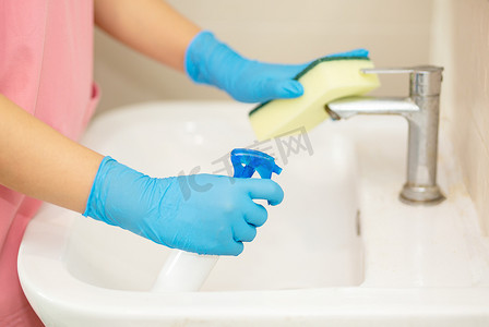 回弹海绵摄影照片_图片中的特写女性手拿蓝色橡胶手套和清洁海绵，取出并清洗浴室水槽和镜子