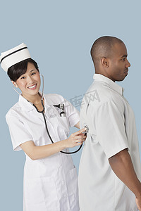 一位快乐的女医生在浅蓝色背景下用听诊器检查男性患者背部的肖像