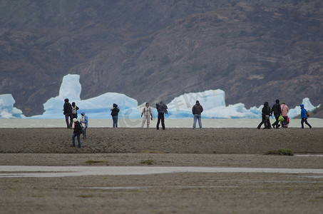 碎片漂浮摄影照片_灰色湖中的游客和背景中的冰山。