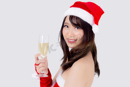 喝饮料女孩摄影照片_美丽的肖像年轻亚洲女人在圣诞老人拿着一杯香槟与派对庆祝圣诞节假期隔离在白色背景，亚洲女孩喝饮料，圣诞节和新年概念。