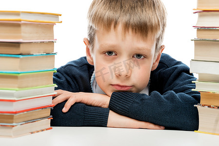一个疲惫的小学生的肖像特写在一堆书中间