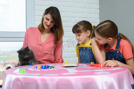 棋盘游戏摄影照片_一家人看着猫玩棋盘游戏桌上的筹码