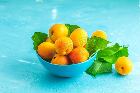 蓝色混凝土苏上蓝色碗中的新鲜甜橙杏