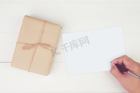 男人用空白贺卡写信，木桌上放着带牛皮纸的礼品盒，礼物和包装，明信片模型，顶视图，平躺，复印空间，假日概念。
