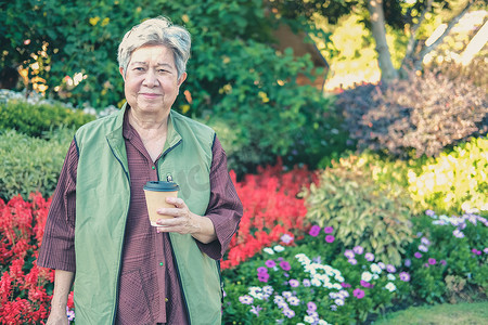 咖啡茶摄影照片_亚洲老年老年妇女在花园里喝咖啡茶。
