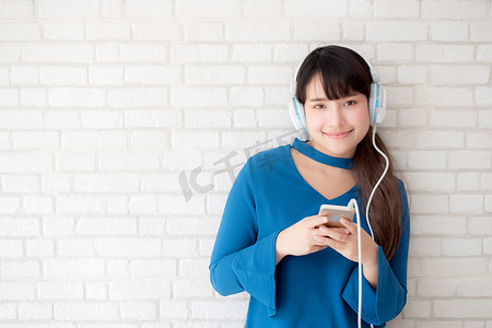 美丽的肖像亚洲年轻女性站在水泥混凝土背景上快乐地享受和享受耳机听音乐，女孩的生活方式用耳机放松收音机，技术概念。