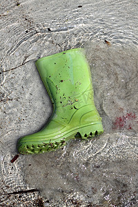 在海滩岸污染的绿色靴子垃圾