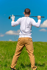 绿色场地摄影照片_高尔夫球手在绿色场地中肩上扛着高尔夫球杆休息