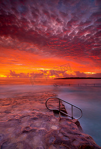 在岩石水池和海洋的富有的红色惊人的日出