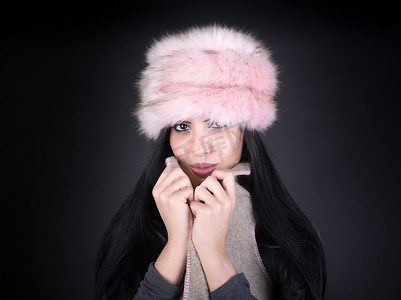 黑色背景上戴着粉红色帽子的年轻女子的冬季肖像