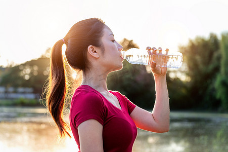 女性喝水摄影照片_在阳光下运动的女人喝水。