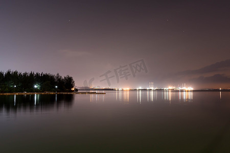 大海黄昏摄影照片_黄昏时分，海、码头、天空的海岸线景观，灯光反射在水面上