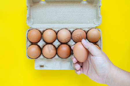 男人的手在纸箱里捡起一个棕色的鸡蛋。