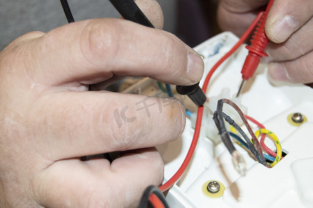电压表摄影照片_老电工手的特写，使用数字电压表电压修复电熨斗，选择性聚焦