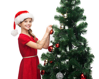 戴着圣诞老人助手帽子的微笑女孩正在装饰一棵树